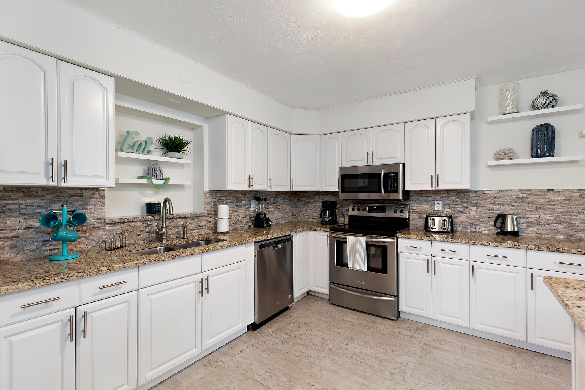 A modern kitchen with white cabinetry, granite countertops, a stainless steel dishwasher, a built-in oven, and a microwave.