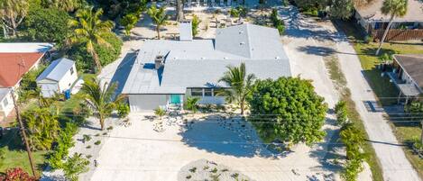 An aerial view of a residential property with a large house, a driveway, and surrounding vegetation.