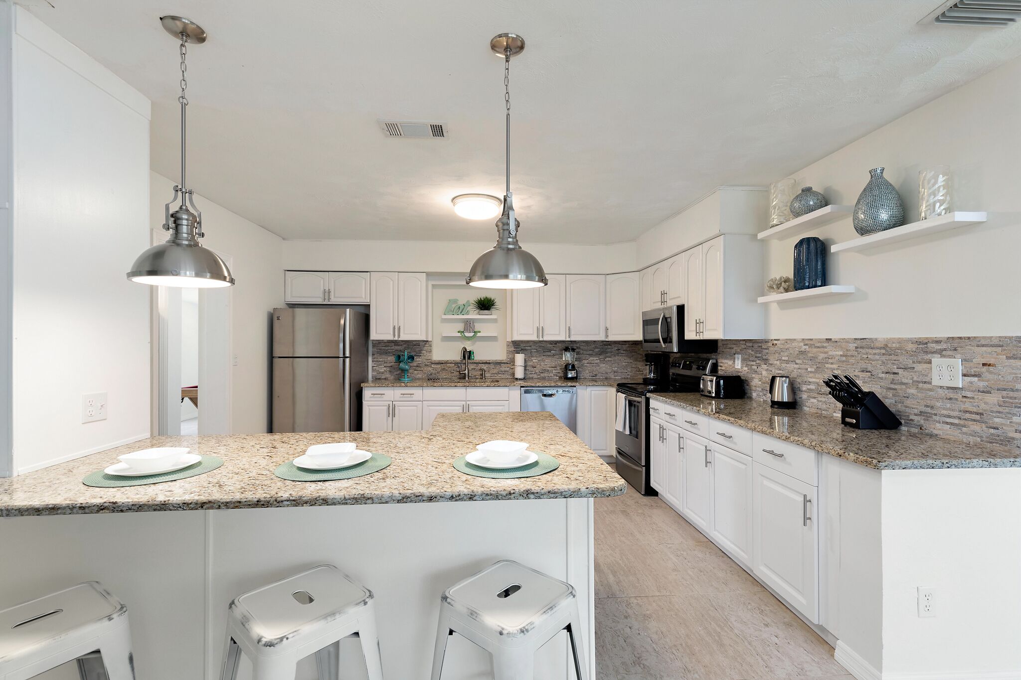 A modern kitchen with granite countertops, white cabinets, stainless steel appliances, and pendant lighting.