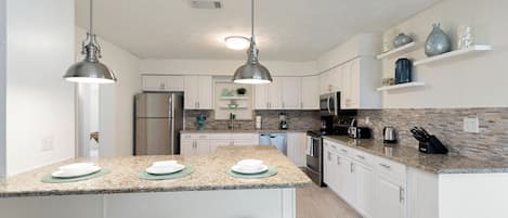 A modern kitchen with granite countertops, white cabinets, stainless steel appliances, and pendant lighting.