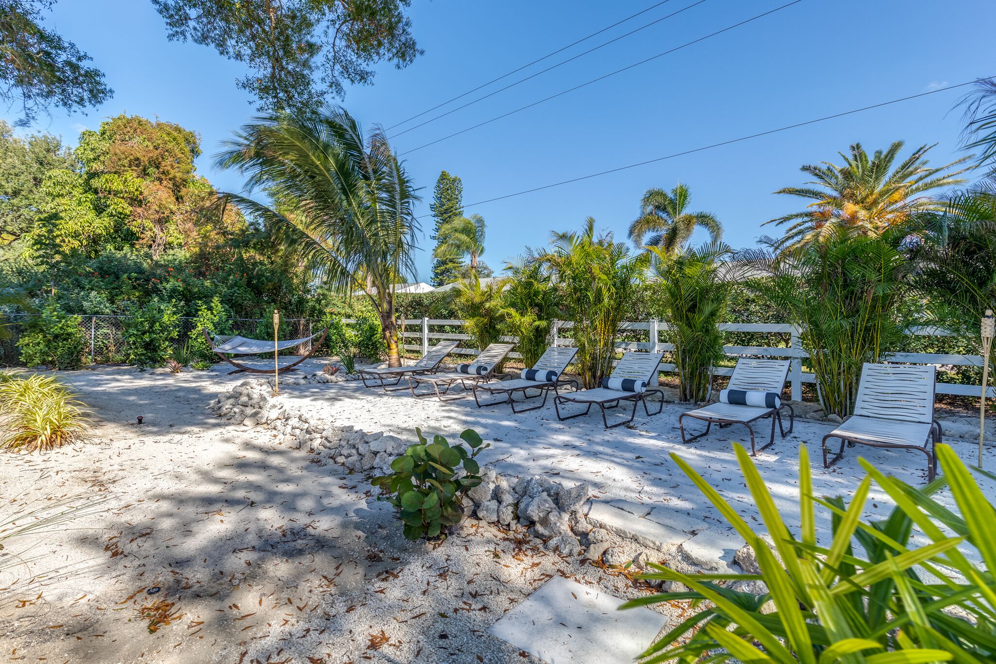 Eine Strandlounge mit Liegestühlen und einer Hängematte, umgeben von üppiger Vegetation und Palmen.
