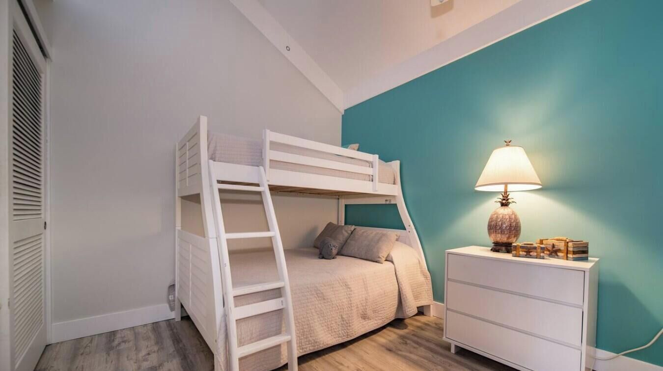 A bunk bed with a ladder, a bedside table with a lamp, and a teal-colored wall.