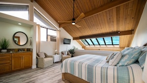 Ein Schlafzimmer mit einem großen Bett, einem Deckenventilator, einem Fernseher und einem Oberlicht.