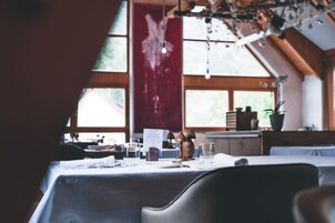 A dining area with tables set for service, a menu stand, and a view of the outdoors through large windows.