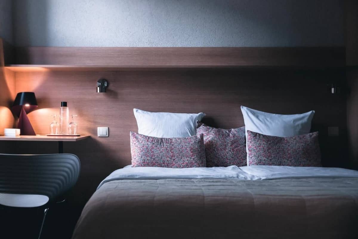 A hotel room with a bed, a bedside table with a lamp, and a chair.