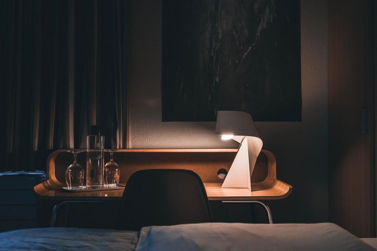 Una habitación de hotel con cama, mesita de noche con lámpara y un cuadro colgado en la pared.