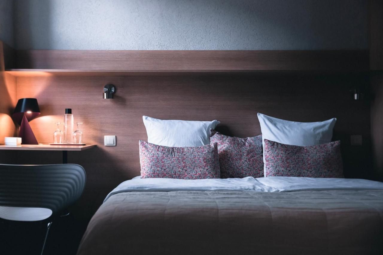A hotel room with a bed, a bedside table with a lamp, and a chair.