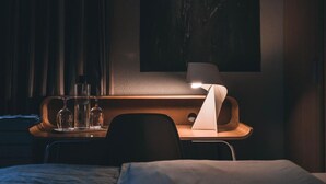 Una habitación de hotel con cama, mesita de noche con lámpara y un cuadro colgado en la pared.