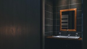 Un baño moderno con baldosas oscuras, un mueble de tocador de madera y un espejo con marco de madera.