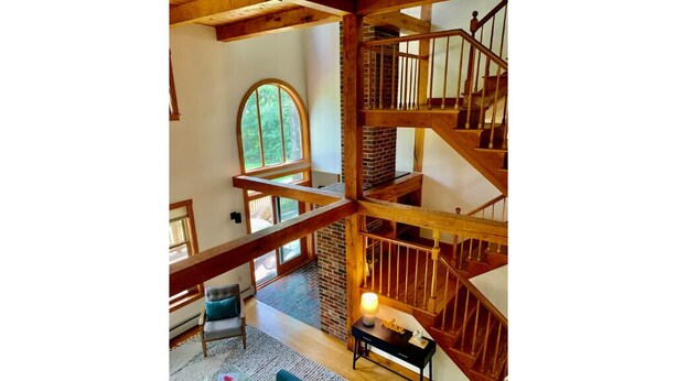 Interior de madera con varios niveles, una escalera, chimenea y un amplio ventanal arqueado.