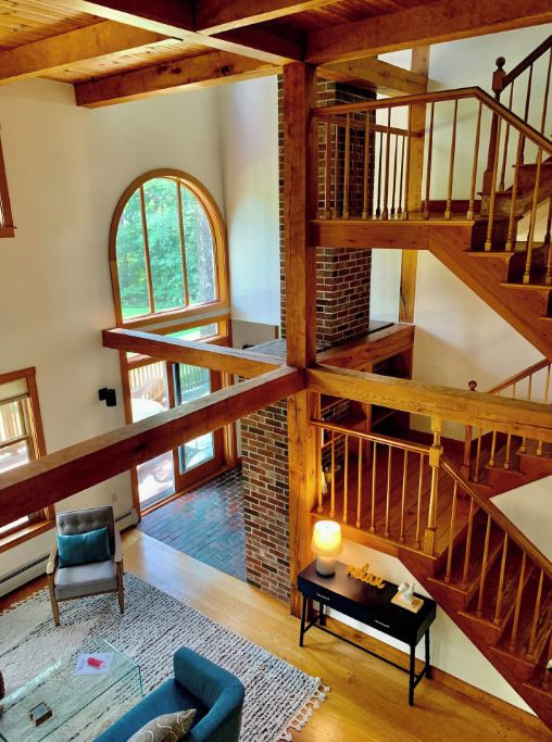 A multi-level wooden interior with a staircase, a fireplace, and a large arched window.