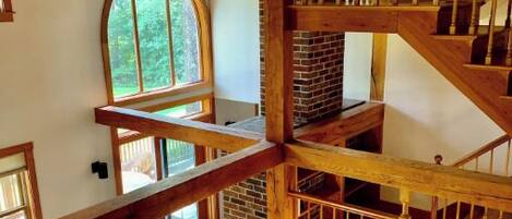 A multi-level wooden interior with a staircase, a fireplace, and a large arched window.