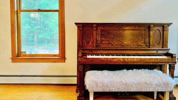 Un pianoforte in legno con una panca in una stanza con una grande finestra.