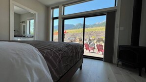 Ein Schlafzimmer mit einem großen Bett, einer Schiebetür zu einem Außenbereich mit Stühlen und Blick auf Berge.
