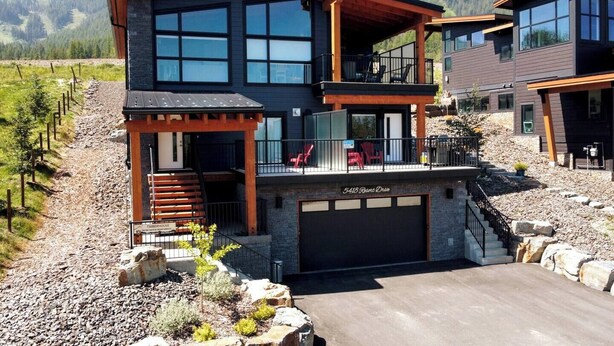 Ein modernes, zweistöckiges Haus mit Garage, überdachter Veranda und Blick auf die Berge.
