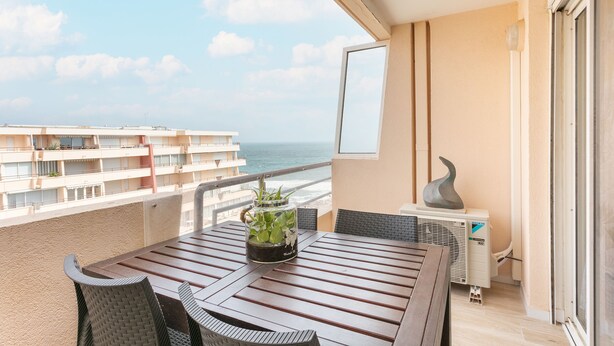 A balcony with a wooden table, chairs, a potted plant, and a view of the ocean. - F3 terrace sea view, swimming pool, parking and air conditioning (Sète)