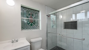 A bathroom with a white sink, toilet, and a glass-enclosed shower with a metal handle. - F1 •  30% OFF • Updated, Cozy & Clean • Fast WiFi • 2BR/2BA Monthly Rental (San Antonio)