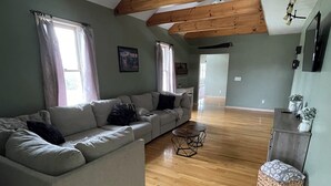 Un espacio habitable amplio con un sofá seccional grande, piso de madera y un techo alto con vigas a la vista.