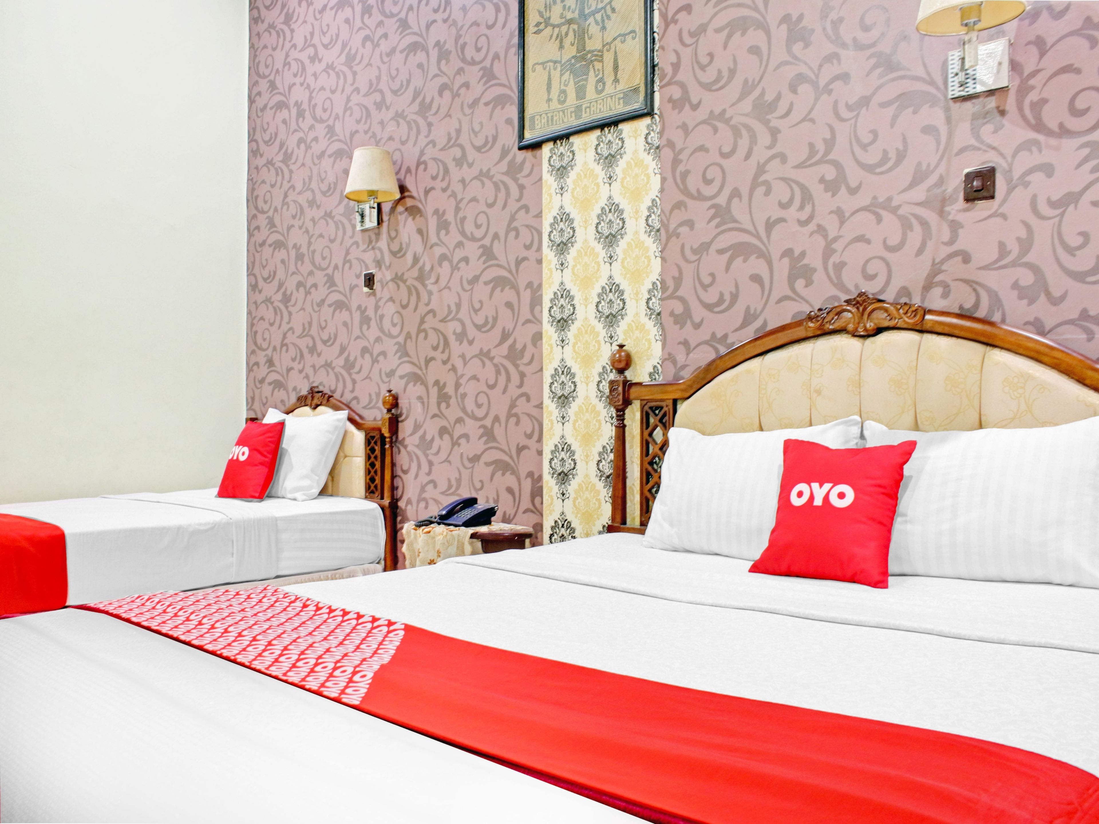 A hotel room with two beds, a red and white bedspread, a telephone on a nightstand, and patterned wallpaper.