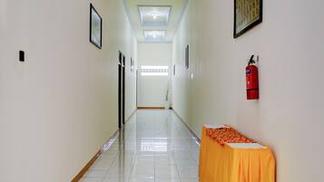 A hallway with a tiled floor, framed pictures on the walls, a fire extinguisher, and a table with a tablecloth.