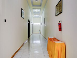 A hallway with a tiled floor, framed pictures on the walls, a fire extinguisher, and a table with a tablecloth. - Capital O 90417 Hotel Batu Suli Internasional (Palangkaraya)