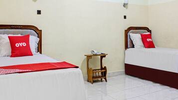 Two beds with red pillows, a bedside table with a phone, and a wall-mounted light fixture.