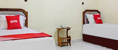 Dos camas con almohadas rojas, una mesita de noche con un teléfono y una lámpara de pared.