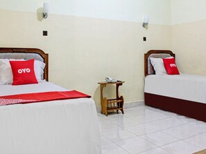 Two beds with red pillows, a bedside table with a phone, and a wall-mounted light fixture. - Capital O 90417 Hotel Batu Suli Internasional (Palangkaraya)