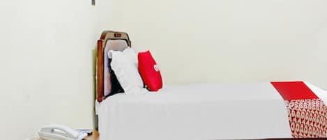 A single bed with a white and red bedspread, a wooden headboard, a red pillow, and a white bedside telephone on a wooden nightstand.
