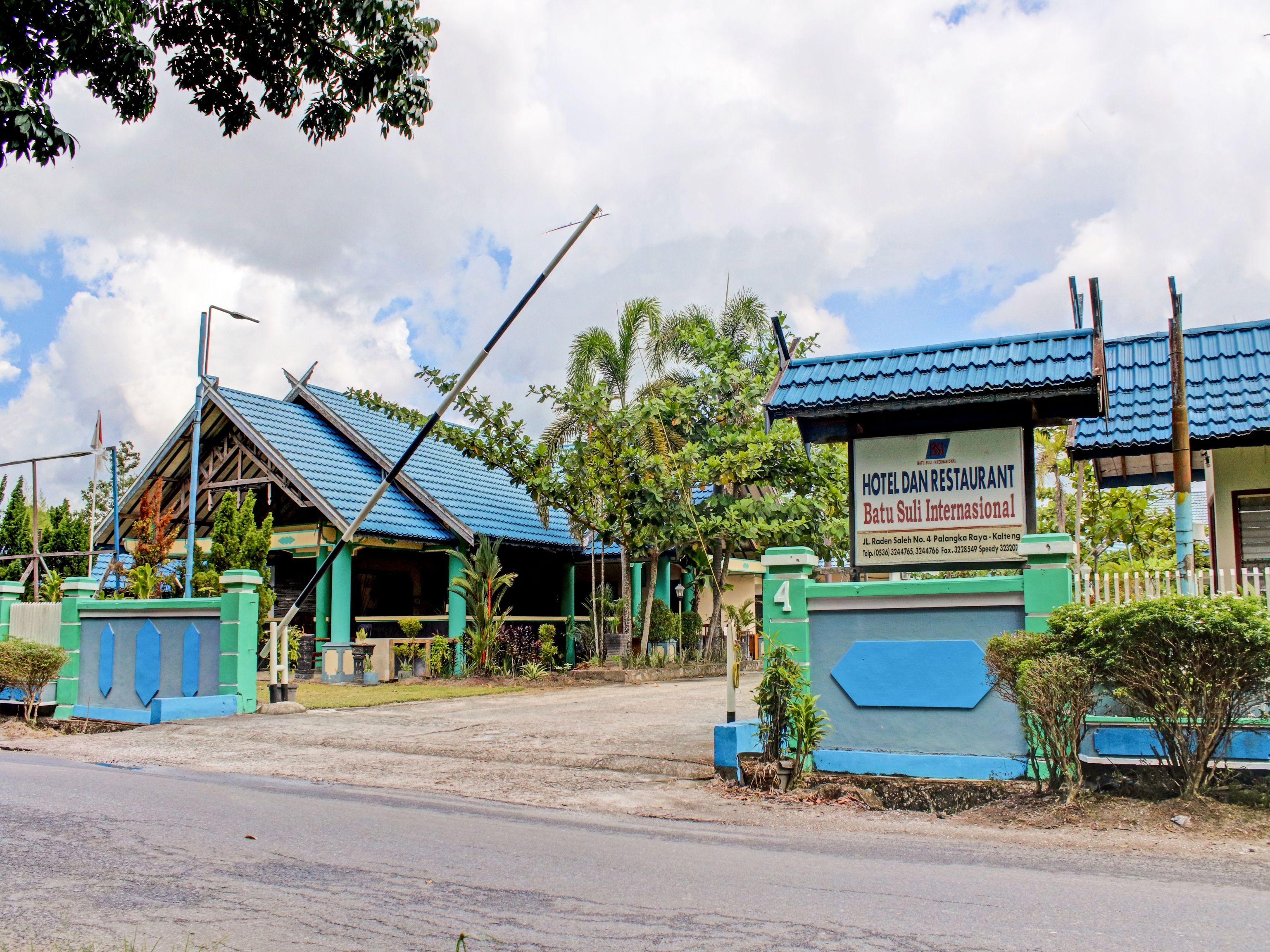 A hotel with a blue roof, a signboard, and a gated entrance.