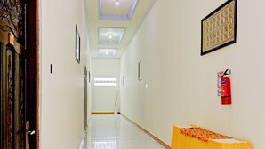 A hallway with a tiled floor, a fire extinguisher, framed artwork, and a table with a yellow tablecloth. - Capital O 90417 Hotel Batu Suli Internasional (Palangkaraya)