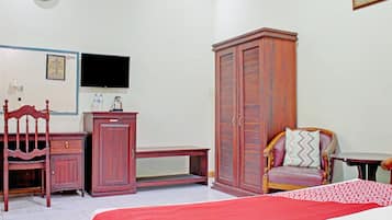 A bedroom with a bed, a wooden wardrobe, a desk, a chair, a television, and a clock on the wall.