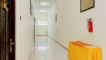 A hallway with a tiled floor, a fire extinguisher, framed artwork, and a table with a yellow tablecloth.