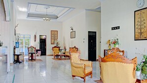 A spacious room with a high ceiling, a chandelier, and a large window. There are several ornate chairs and a wooden table. - Capital O 90417 Hotel Batu Suli Internasional (Palangkaraya)