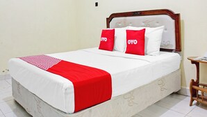 A bed with a white and red bedspread, two red pillows with 'OYO' text, a wooden headboard, and a small wooden table with a phone. - Capital O 90417 Hotel Batu Suli Internasional (Palangkaraya)