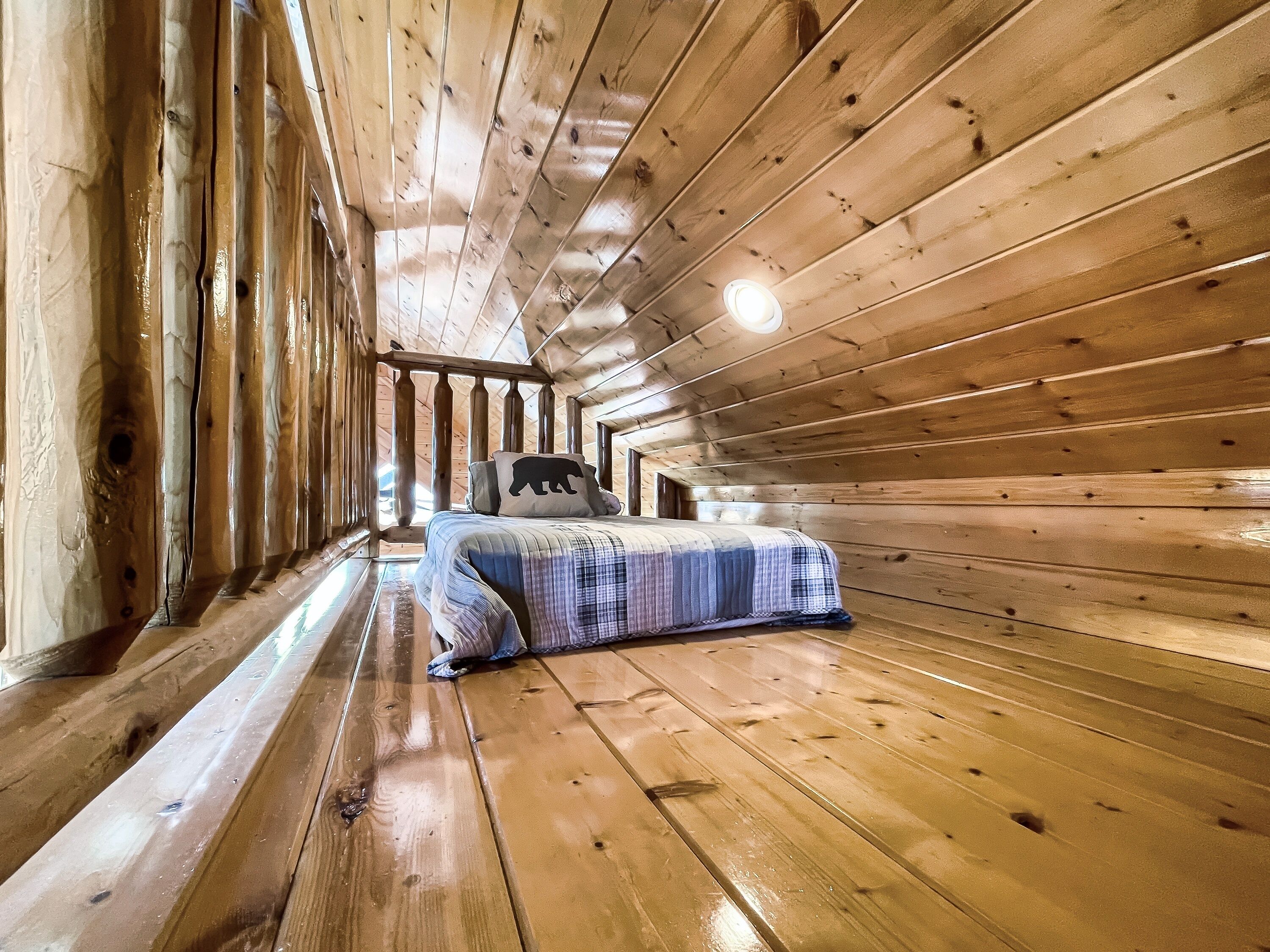 Ein Interieur einer Holzhütte mit einem Bett, einem Hollerker und einer Deckenleuchte.