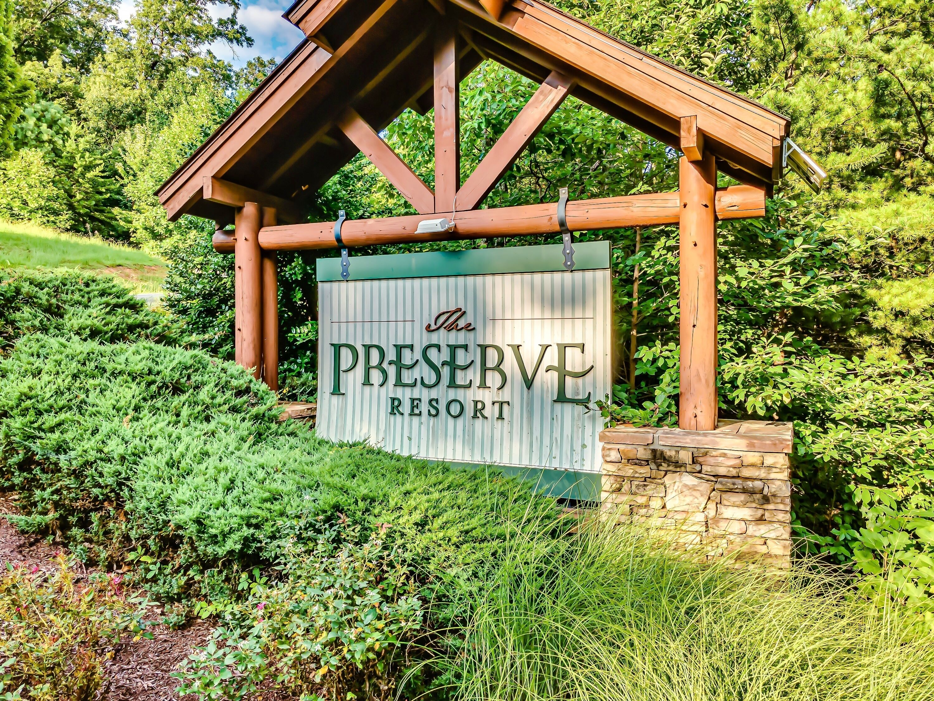 A wooden sign with the text "The Preserve Resort" against a backdrop of lush greenery and a stone wall.