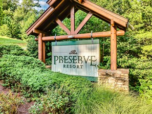 Une enseigne en bois portant l’inscription « The Preserve Resort », avec en arrière-plan une végétation luxuriante et un mur de pierres.