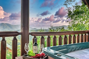 Un balcon avec une balustrade en bois, une table avec une bouteille de vin, un verre et une assiette de raisins.