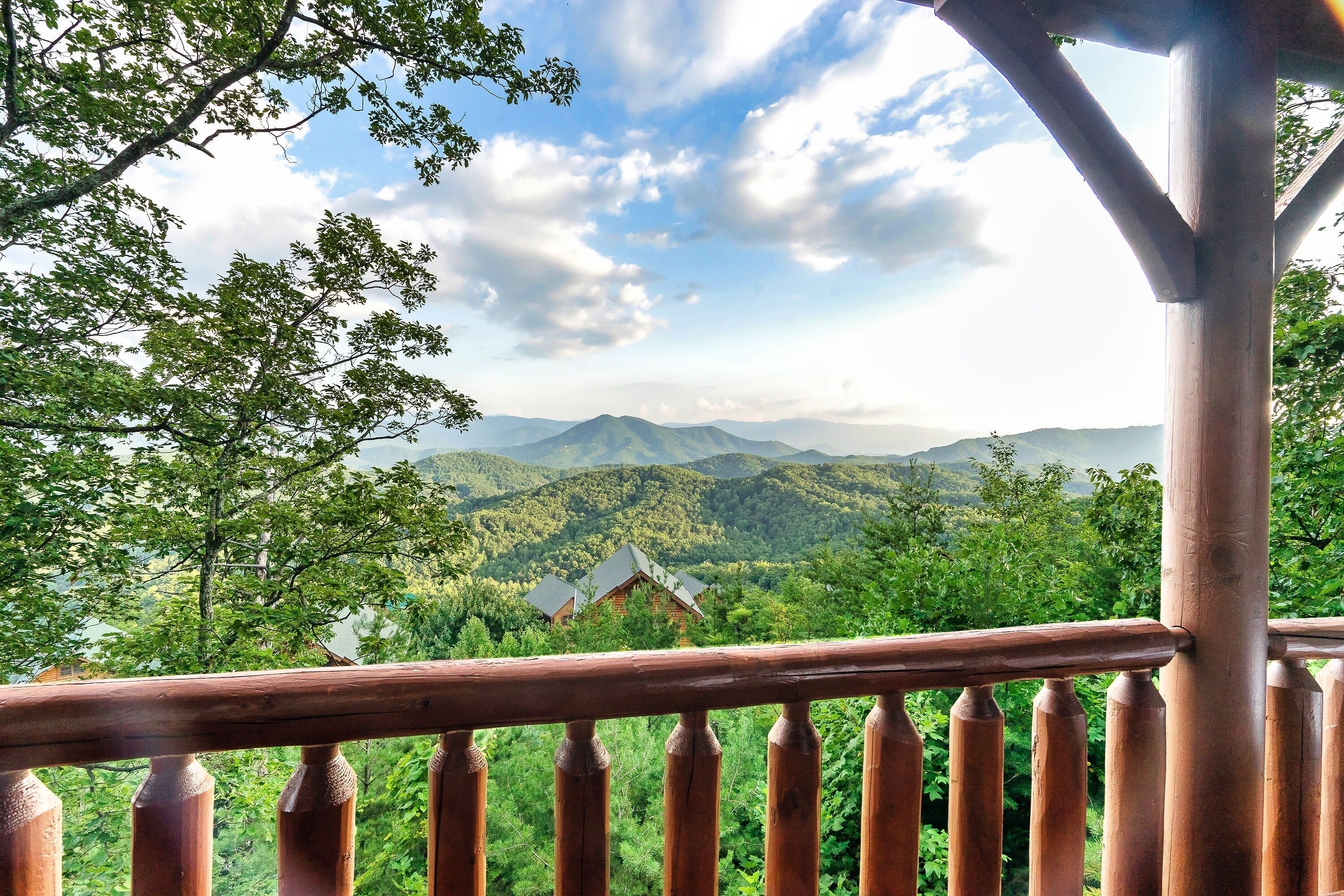 A wooden balcony with a view of a mountainous landscape and a house in the distance.