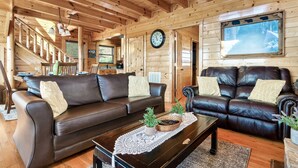 L’intérieur chaleureux d’un chalet avec des murs en bois, un canapé en cuir marron, un fauteuil assorti, une table basse en bois et une grande fenêtre donnant sur un paysage enneigé.