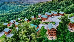 Un chalet doté de plusieurs cabanes, entouré d’une forêt dense, avec en toile de fond un paysage montagneux.