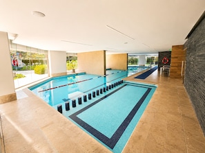 An indoor swimming pool with clear lanes, a lifeguard chair, and a view of greenery outside.