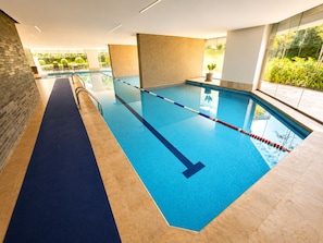 Une piscine intérieure avec des couloirs bien délimités, un sol bleu et une vue sur la verdure environnante.