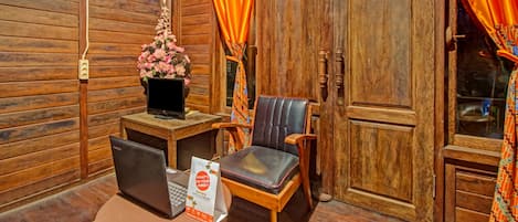 A wooden interior with a desk, two chairs, a laptop, a vase with flowers, and a door with curtains.