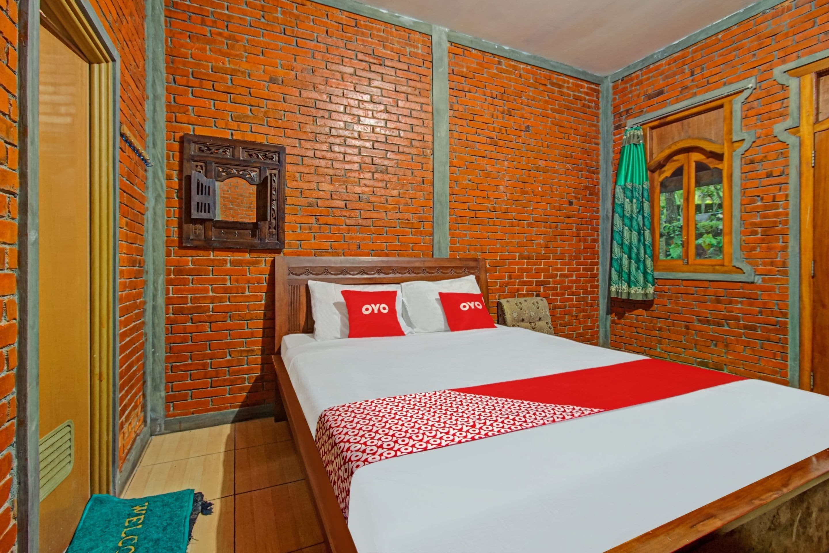 Una habitación con pared de ladrillo, cama con ropa de cama blanca y roja, y felpudo verde.