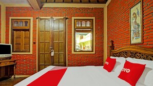 A hotel room with a brick wall, wooden doors, a bed with red pillows, and a television on a wooden stand. - OYO 90031 Villa Papada (Batu)