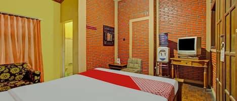 A hotel room with a bed, a television, a small table, a chair, and a wardrobe.