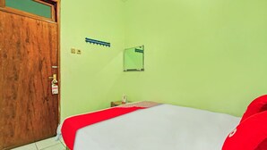 A room with a wooden door, a bed with a red and white bedspread, a small bedside table with a lamp, and a wall-mounted mirror. - OYO 90031 Villa Papada (Batu)
