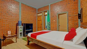 Ein Zimmer mit Backsteinwand, einem Bett mit weißer und roter Bettwäsche, einer Holzbank, einem kleinen Tisch und einem Fernseher.